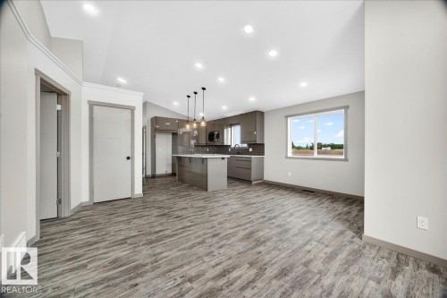 Open-concept living space featuring wood-finish flooring, recessed lighting, and a modern kitchen with a central island - 1 Whitetail Way, Mundare, AB 
