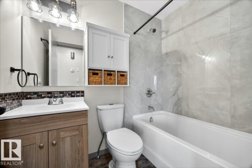 Full bathroom featuring a white bathtub, large format stone-look tile shower surround, wood-finish vanity with an integrated sink, and a framed mirror - 1 Whitetail Way, Mundare, AB 