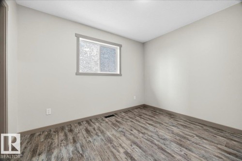 Spacious room featuring light neutral wall paint, wood-finish flooring, and a single window with gray trim - 1 Whitetail Way, Mundare, AB 
