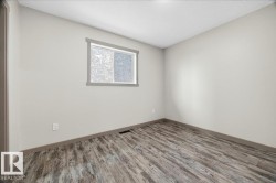 Spacious room featuring light neutral wall paint, wood-finish flooring, and a single window with gray trim - 