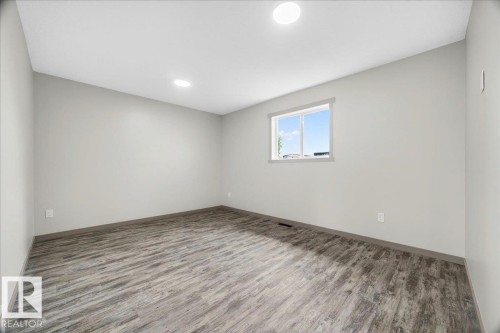 Spacious room featuring wood-finish flooring, a contemporary window, recessed ceiling lighting, and neutral wall paint - 1 Whitetail Way, Mundare, AB 