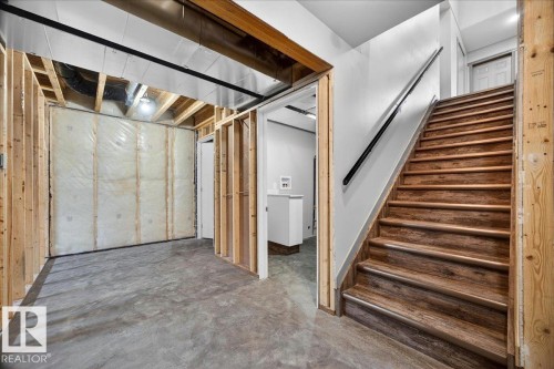 Lower-level space featuring wood-finish stairs with a black handrail, exposed ceiling joists, and a concrete floor - 1 Whitetail Way, Mundare, AB 