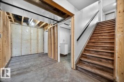 Lower-level space featuring wood-finish stairs with a black handrail, exposed ceiling joists, and a concrete floor - 