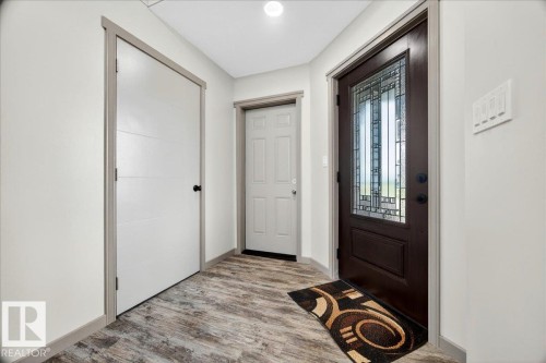Entryway featuring a dark wood-finish door with decorative glass, wood-finish flooring, and light-toned walls - 1 Whitetail Way, Mundare, AB 