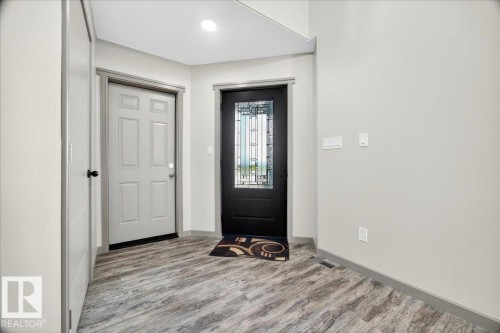Entryway featuring a dark paneled door with decorative glass, a light paneled door, wood-finish flooring, and light gray wall paint with matching trim - 1 Whitetail Way, Mundare, AB 