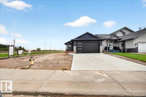 Modern exterior with a clean-lined garage door featuring frosted glass panels, an extended concrete driveway, and a front entrance with dark steps - 1 Whitetail Way, Mundare, AB 