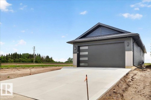 Contemporary exterior featuring dark gray siding, a prominent gable roof, and a modern garage door with integrated horizontal windows - 1 Whitetail Way, Mundare, AB 