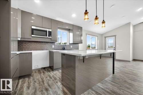 Contemporary kitchen featuring sleek gray cabinetry, a tile backsplash, and wood-finish flooring - 1 Whitetail Way, Mundare, AB 