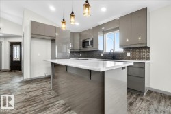 Contemporary kitchen featuring high-gloss gray cabinetry, a white countertop island with seating, a black patterned backsplash, and stainless steel appliances - 
