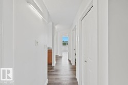 Hallway with wood-finish flooring, white walls, and bright overhead lighting - 