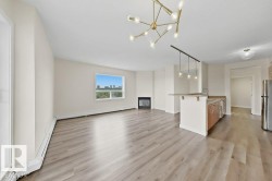 Open-concept living area with light wood-finish flooring, a modern brass chandelier, and a built-in fireplace - 