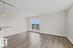 Expansive room featuring wood-finish flooring, a contemporary chandelier, a sliding glass door to a balcony, and abundant natural light - 