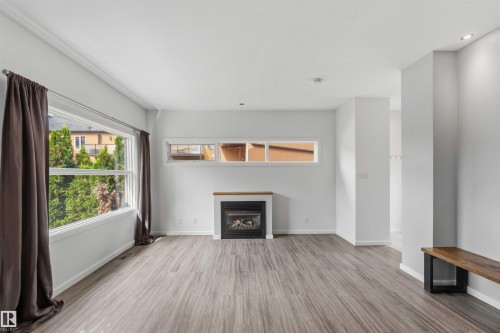 Spacious room featuring wood-finish flooring, white walls, and a gas fireplace with a wood mantle - 1 14315 Stony Plain, Edmonton, AB 