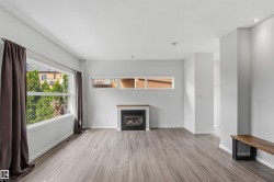 Spacious room featuring wood-finish flooring, white walls, and a gas fireplace with a wood mantle - 