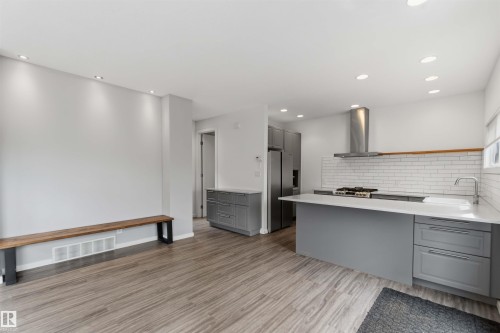 Open-concept kitchen featuring gray cabinetry, stainless steel appliances, a white subway tile backsplash, and light-toned countertops - 1 14315 Stony Plain, Edmonton, AB 