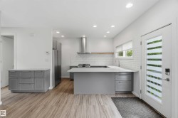 Modern kitchen with light grey cabinetry, stainless steel appliances, and wood-finish flooring - 