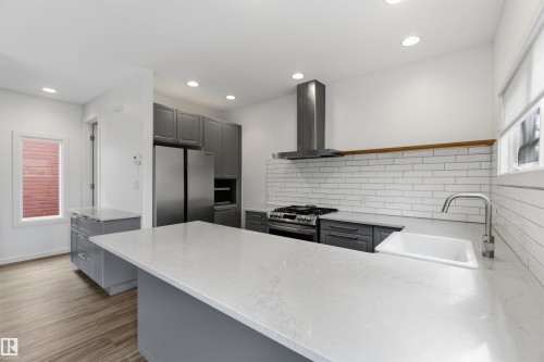 Contemporary kitchen featuring a large central island with a solid surface countertop, stainless steel appliances, grey cabinetry, white subway tile backsplash, and wood-finish flooring - 1 14315 Stony Plain, Edmonton, AB 