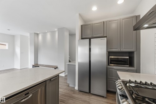 Modern kitchen featuring gray cabinetry, stainless steel appliances, and wood-finish flooring - 1 14315 Stony Plain, Edmonton, AB 