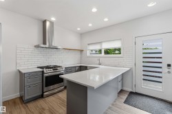 Kitchen featuring gray cabinetry, light countertops, a subway tile backsplash, a stainless steel range with a ventilation hood, and wood-finish flooring - 