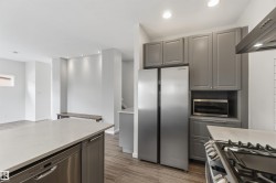 Modern kitchen featuring gray cabinetry, stainless steel appliances, and wood-finish flooring - 