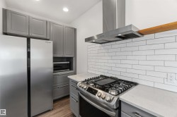 Modern kitchen featuring stainless steel appliances, shaker-style cabinetry, a subway tile backsplash, light-toned countertops, and wood-finish flooring - 