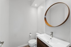Modern powder room featuring a wall-mounted round mirror with a wood-tone frame, a rectangular vanity with a white basin sink, a brushed nickel faucet, and wood-finish flooring - 