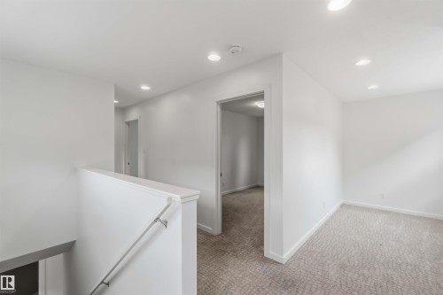 Upper-level landing featuring a white painted railing, recessed lighting, and light-toned patterned carpeting - 1 14315 Stony Plain, Edmonton, AB 