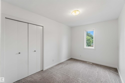 Spacious room featuring white walls, gray patterned carpet, a single window, white bi-fold closet doors, and a flush-mount ceiling light fixture - 1 14315 Stony Plain, Edmonton, AB 