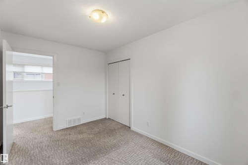 Neutral-toned room featuring a white ceiling and walls, light-colored patterned carpet, a built-in closet with bi-fold doors, and a ceiling-mounted light fixture - 1 14315 Stony Plain, Edmonton, AB 