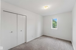 Spacious room featuring white walls, gray patterned carpet, a single window, white bi-fold closet doors, and a flush-mount ceiling light fixture - 