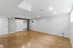 Spacious room featuring wood-finish flooring, recessed lighting, a built-in wardrobe with sliding doors and integrated shelving, and a white interior door with a contemporary handle - 
