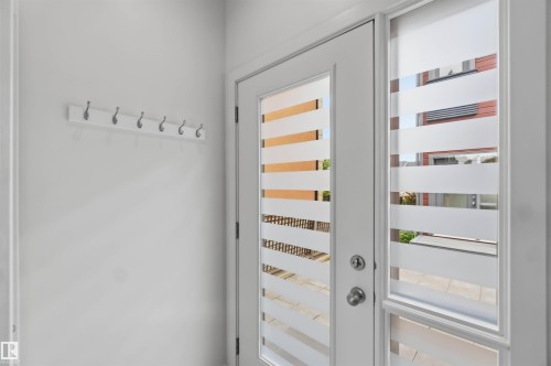 Entryway featuring a white door with frosted horizontal glass panels, a matching sidelight, and a white coat rack with six silver hooks - 1 14315 Stony Plain, Edmonton, AB 