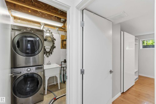 Dedicated laundry area featuring a stacked washer and dryer, utility sink, and tile flooring - 1 14315 Stony Plain, Edmonton, AB 