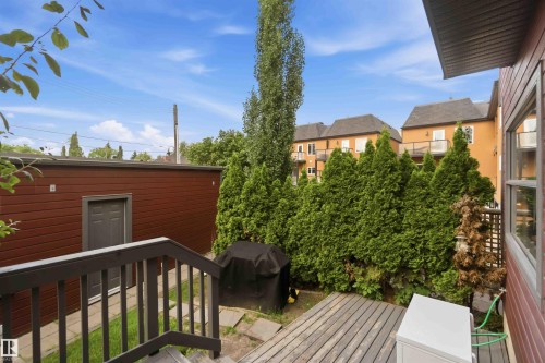Outdoor wooden deck leading to a patio area with a privacy fence and mature evergreen trees - 1 14315 Stony Plain, Edmonton, AB 
