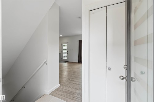 Entryway featuring wood-finish flooring, a white bi-fold closet door, and a modern main entrance door with horizontal glass panels - 1 14315 Stony Plain, Edmonton, AB 