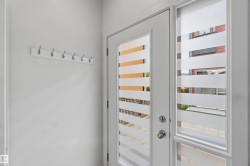Entryway featuring a white door with frosted horizontal glass panels, a matching sidelight, and a white coat rack with six silver hooks - 