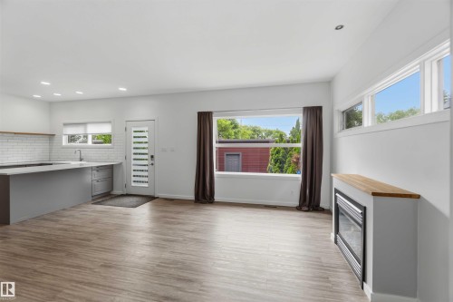 Open-concept living space featuring wood-finish flooring, a modern kitchen island with an undermount sink, a subway tile backsplash, and recessed lighting - 1 14315 Stony Plain, Edmonton, AB 