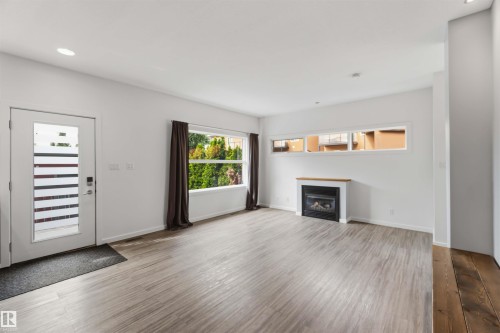 Spacious living area featuring wood-finish flooring, a fireplace with a wood mantle, and multiple windows providing natural light - 1 14315 Stony Plain, Edmonton, AB 