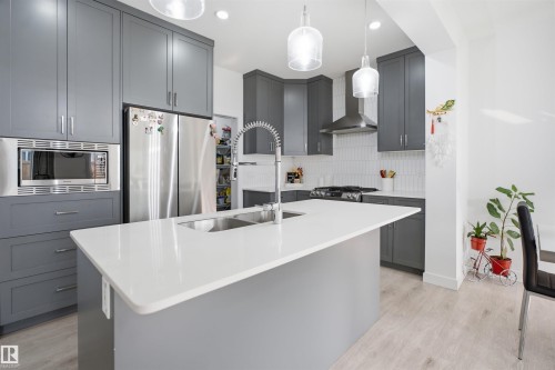 Contemporary kitchen featuring an island with a double basin sink, light-toned cabinetry, stainless steel appliances, a tile backsplash, and light wood-finish flooring - 2508 193 Street, Edmonton, AB 