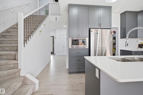 Contemporary kitchen featuring a large island with dual sinks, sleek grey cabinetry, a built-in microwave, and stainless steel appliances - 2508 193 Street, Edmonton, AB 