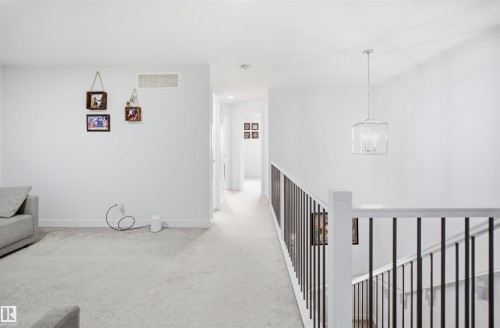 Upper-level landing featuring light-toned carpet flooring, white walls, and a contemporary chandelier - 2508 193 Street, Edmonton, AB 