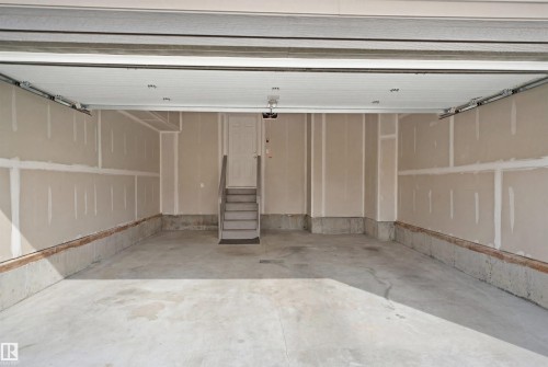 Spacious garage featuring a concrete floor, unfinished drywall, and a direct entry door with stairs - 2508 193 Street, Edmonton, AB 