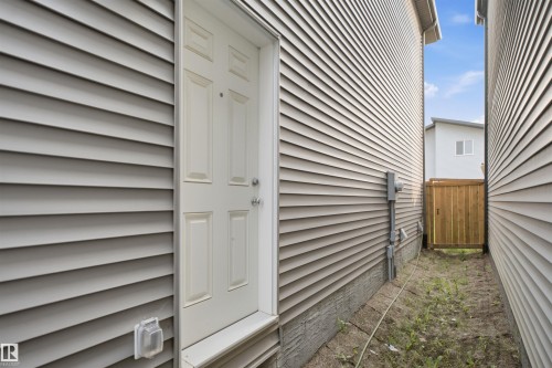 Exterior side entrance featuring a panel door, light gray horizontal siding, and a protected outdoor electrical outlet - 2508 193 Street, Edmonton, AB 