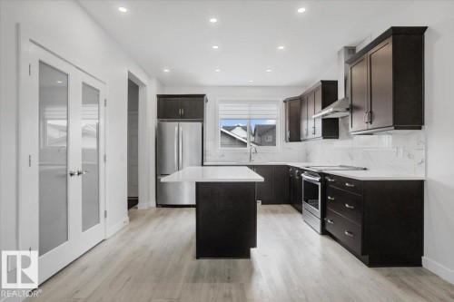 Contemporary kitchen featuring dark wood cabinetry, stainless steel appliances, a center island with white countertop, and white subway tile backsplash - 2852 Duke Crescent, Edmonton, AB 