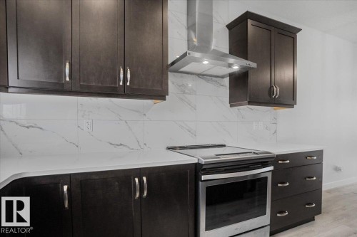 Contemporary kitchen featuring dark wood cabinetry, white countertops, a white tile backsplash with grey veining, a stainless steel range, and a coordinating stainless steel range hood - 2852 Duke Crescent, Edmonton, AB 