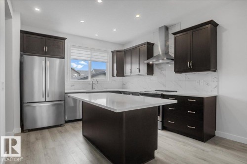 Modern kitchen featuring a central island with a white countertop, dark wood-finish cabinetry, stainless steel appliances, a tile backsplash, and wood-finish flooring - 2852 Duke Crescent, Edmonton, AB 