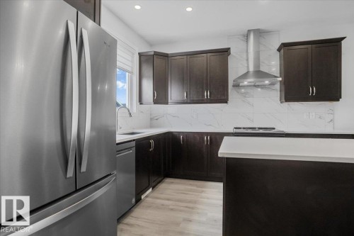 Kitchen featuring dark wood cabinetry, white countertops, stainless steel appliances, and a marble-look tile backsplash - 2852 Duke Crescent, Edmonton, AB 