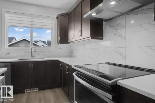 Modern kitchen featuring dark wood-finish cabinetry, white countertops, and a white marble-look tile backsplash - 2852 Duke Crescent, Edmonton, AB 