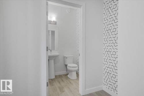 Powder room featuring a pedestal sink, toilet, wood-finish flooring, and a decorative accent wall with a geometric pattern - 2852 Duke Crescent, Edmonton, AB 