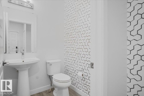 Pedestal sink with chrome faucet and mirror, complemented by a contemporary hexagonal pattern accent wall - 2852 Duke Crescent, Edmonton, AB 